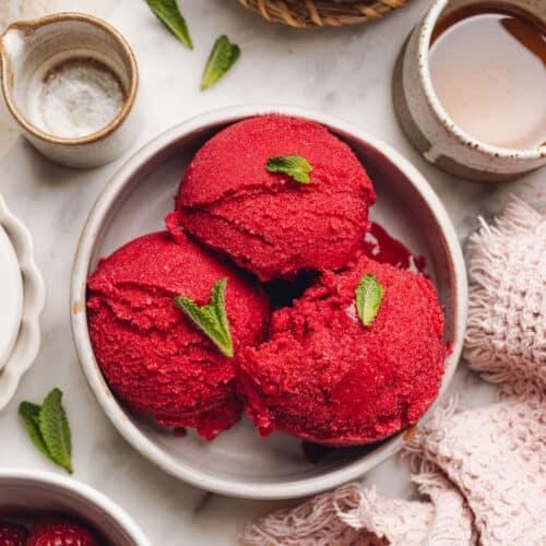 a bowl with scoops of raspberry sorbet with mint leaves on top.