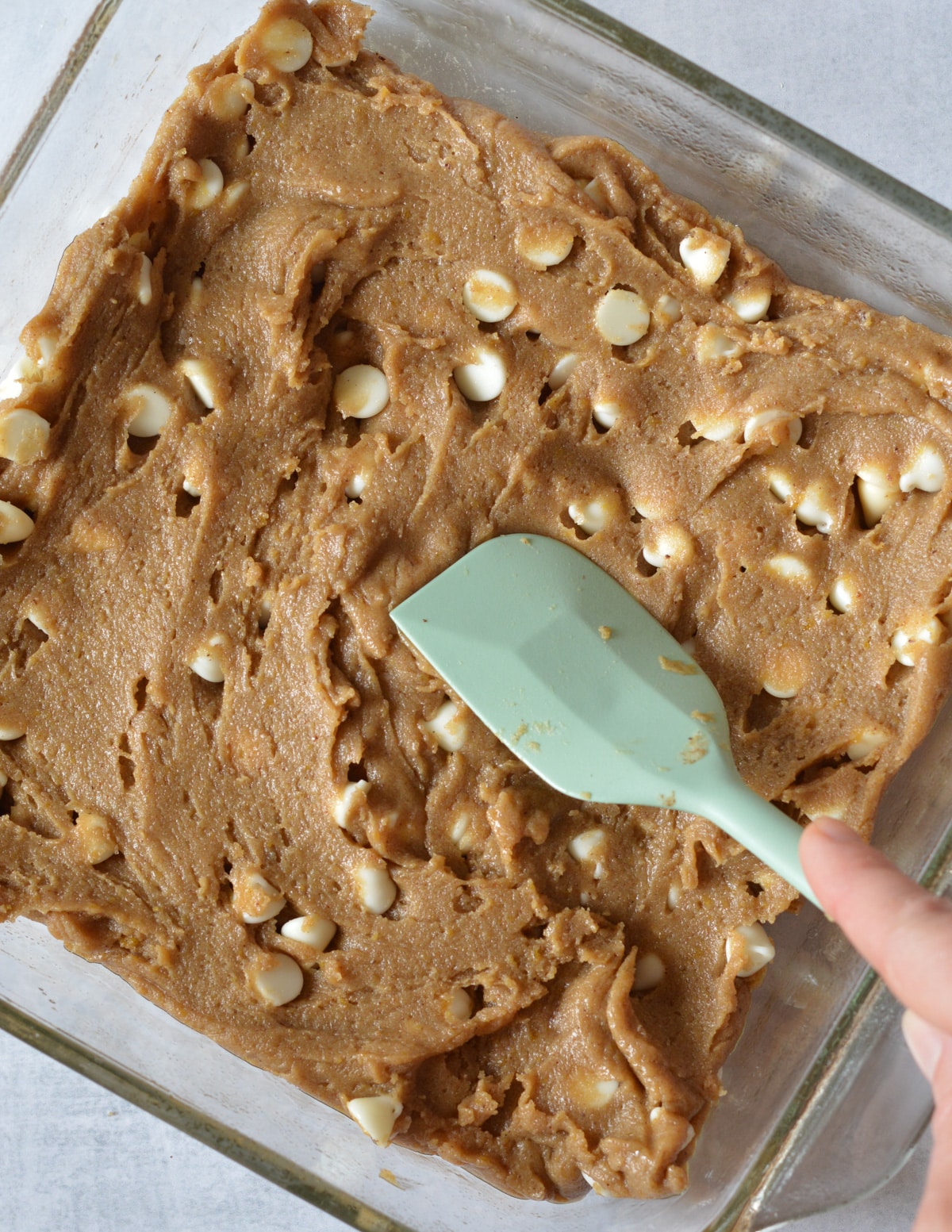spatula spreading gluten free brownie dough into a glass baking dish.