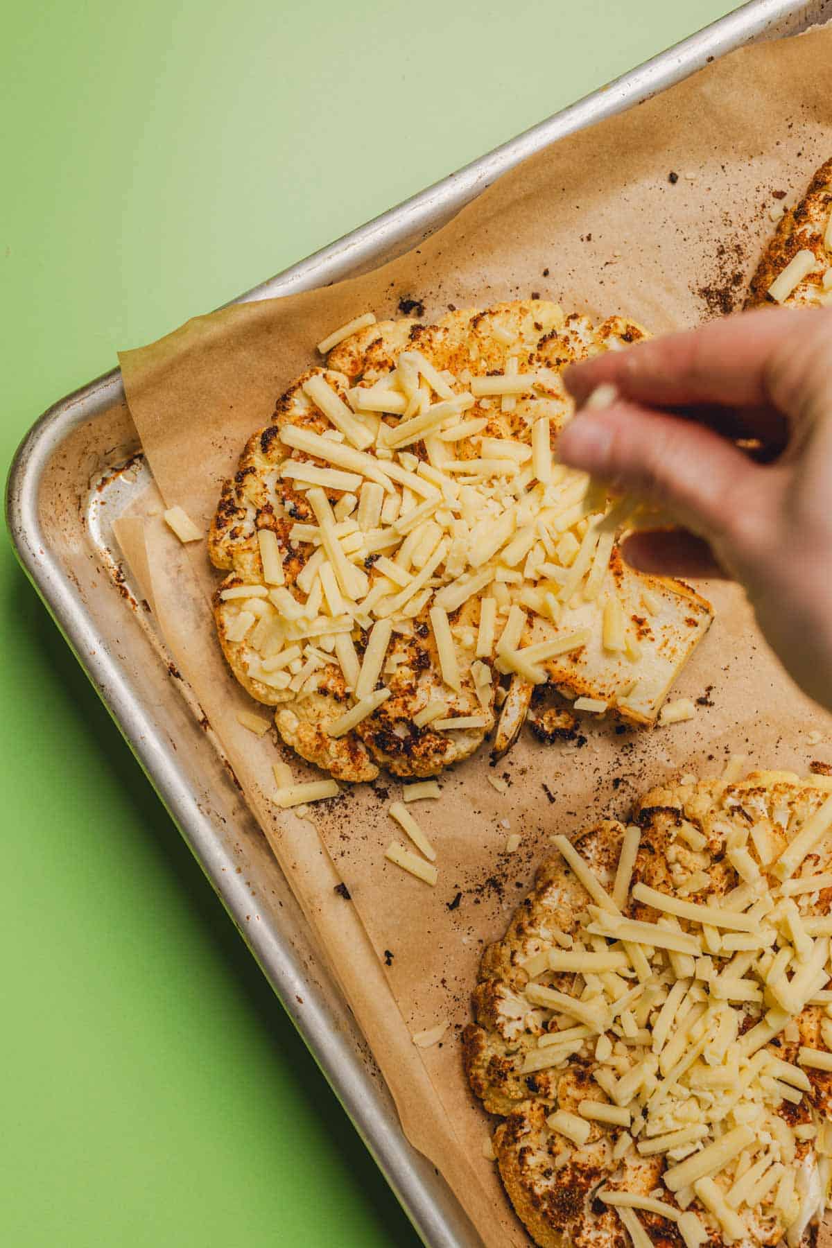 sprinkling shredded gouda cheese on roasted cauliflower steaks