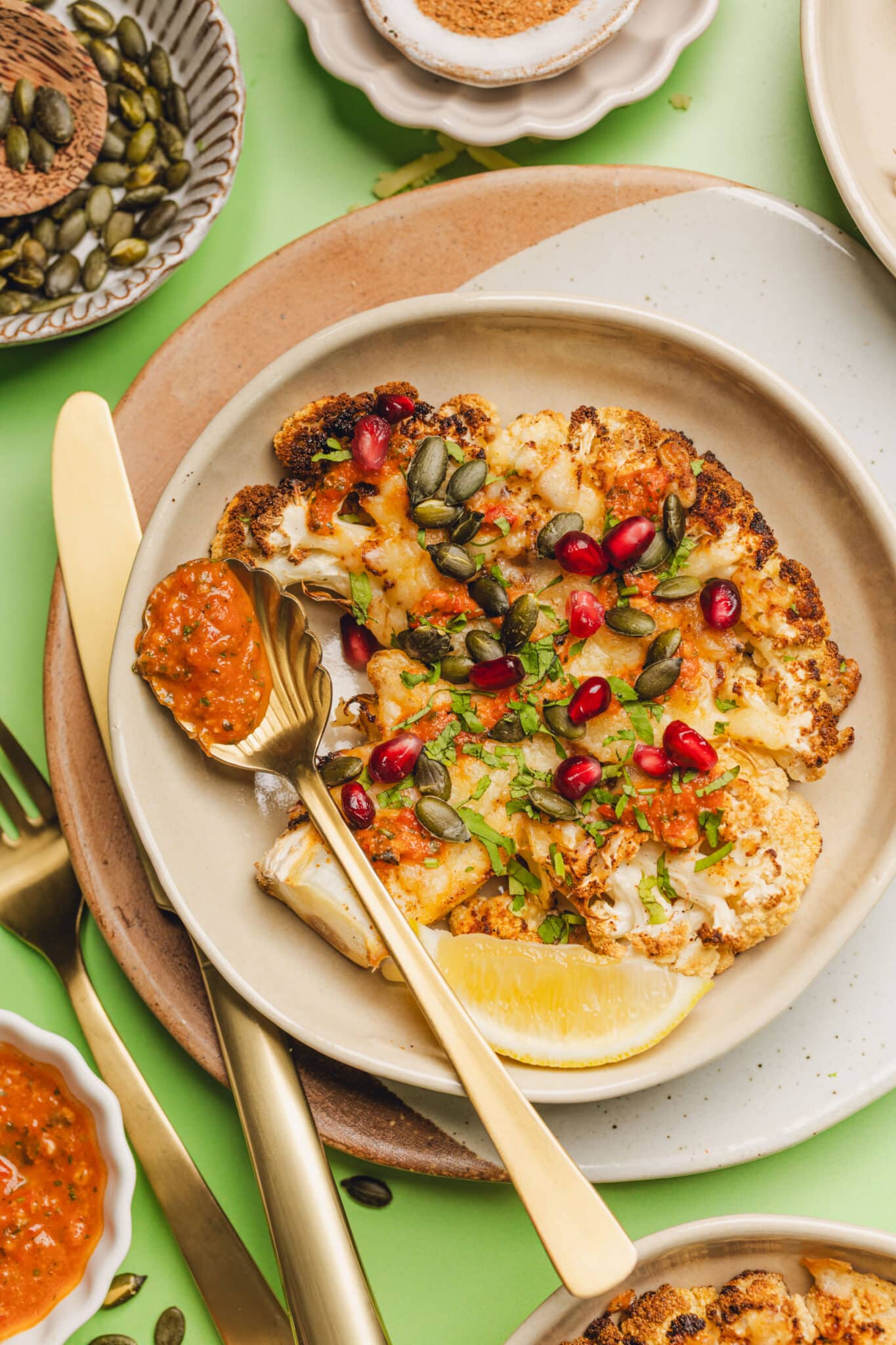 cheesy cauliflower steak with pepitas, cilantro, and pomegranate seeds on top.