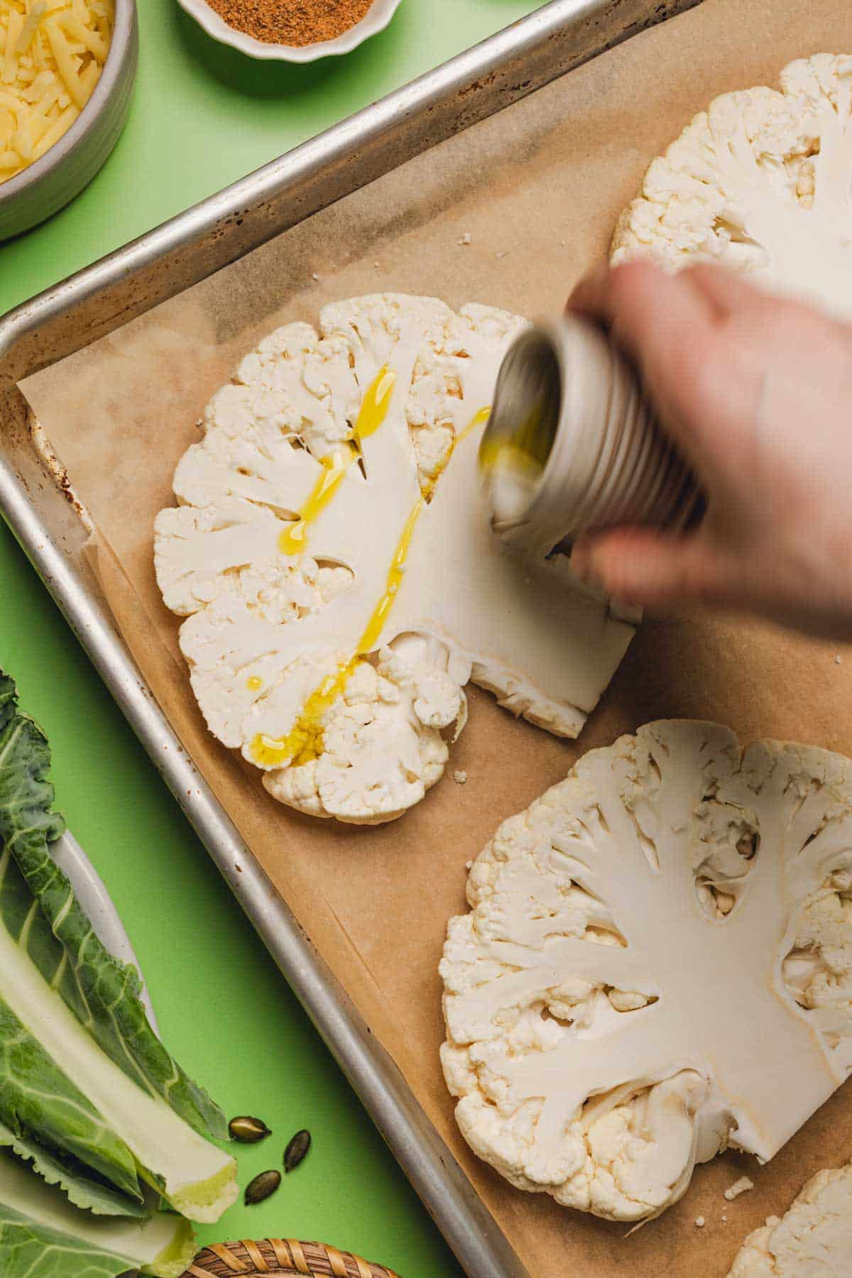 drizzling olive oil onto slices of cauliflower on a sheet pan.