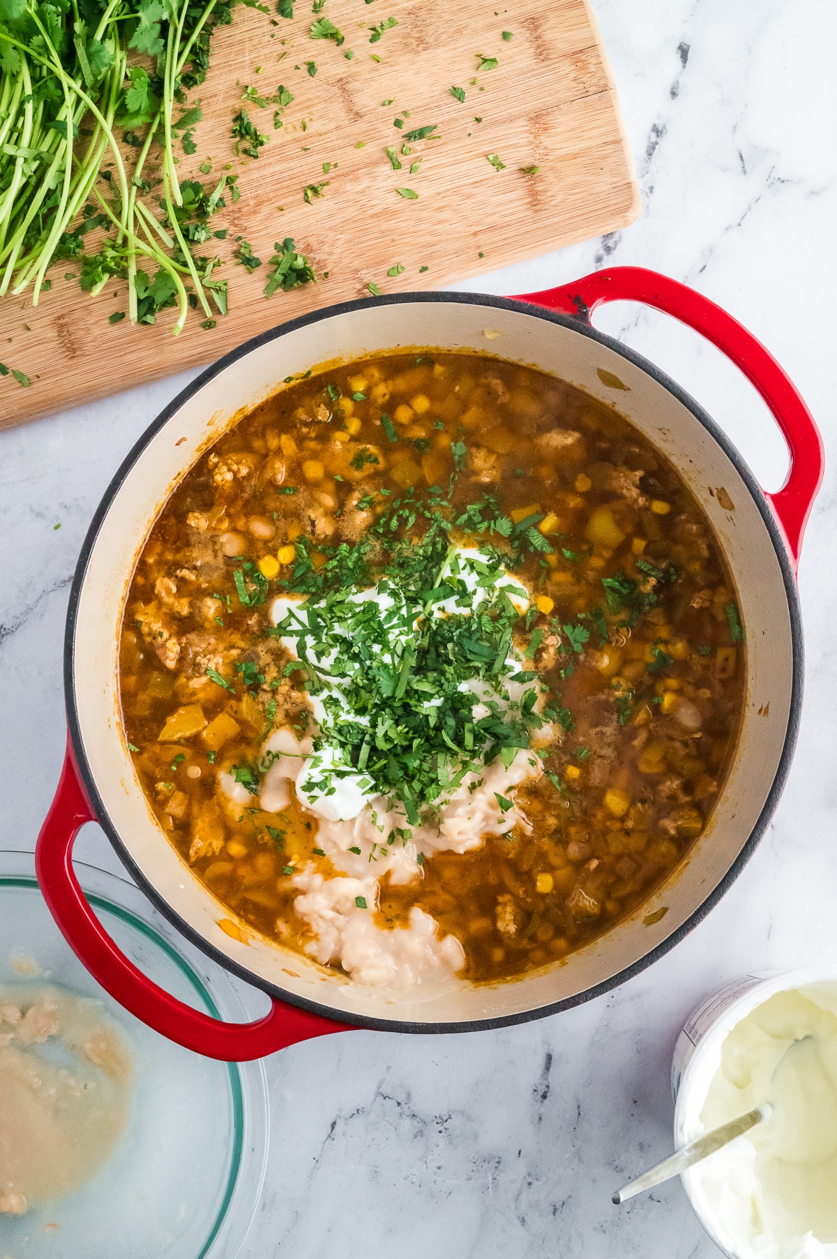 a bowl of chicken chili with sour cream, cilantro, and mashed beans on top.