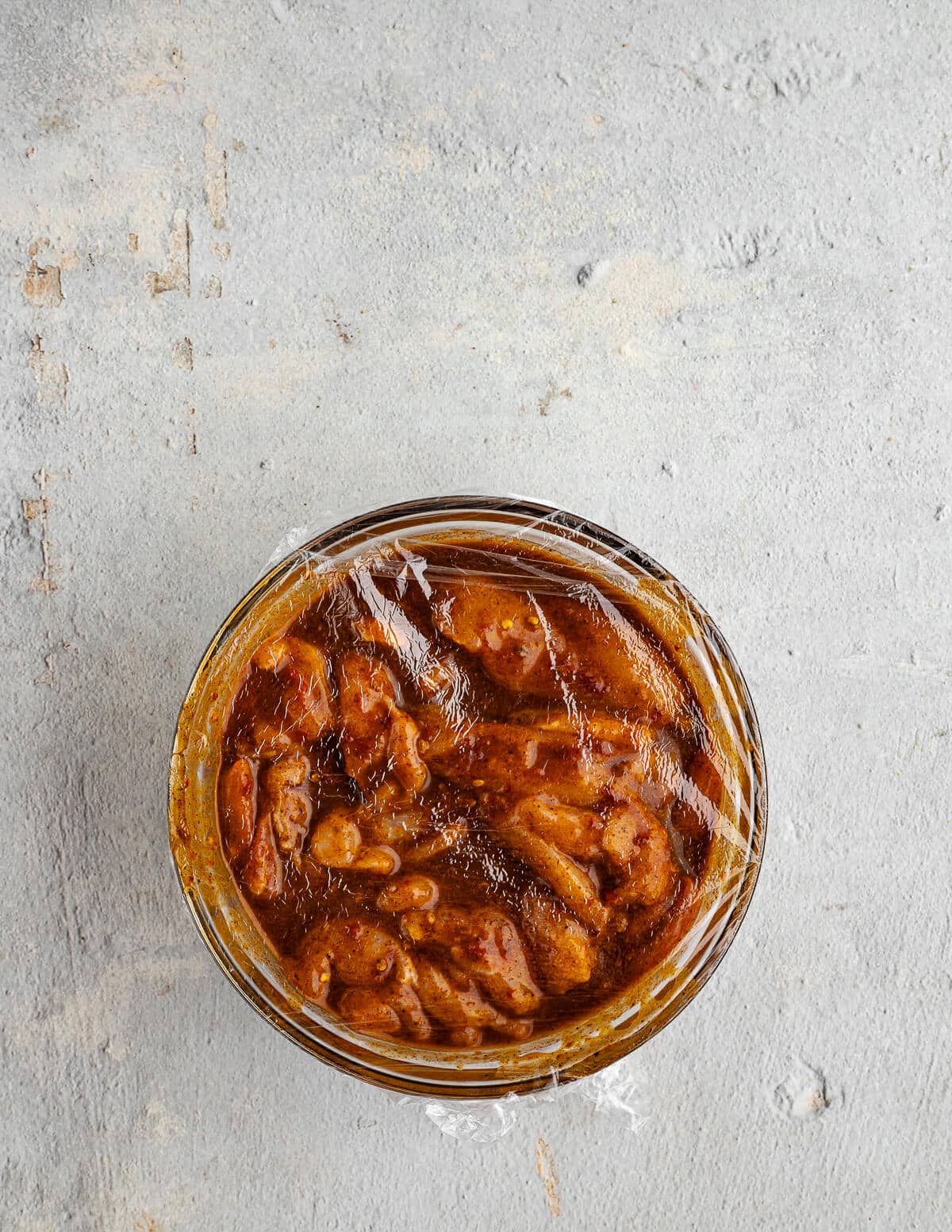a bowl of chicken thighs in a chipotle marinade with saran wrap on top.
