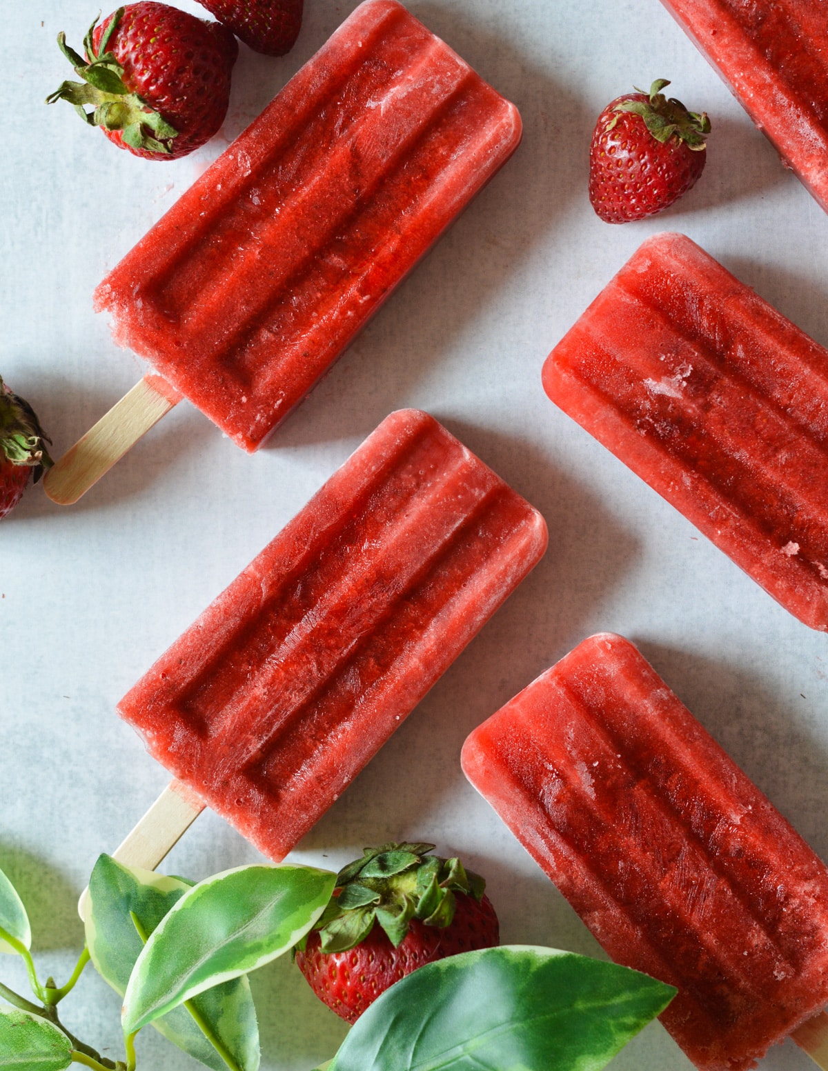 strawberry popsicles on a counter near fresh strawberries.