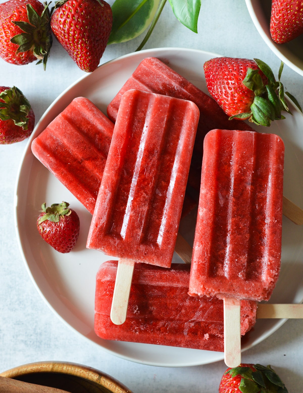 strawberry popsicles on a plate with fresh strawberries.