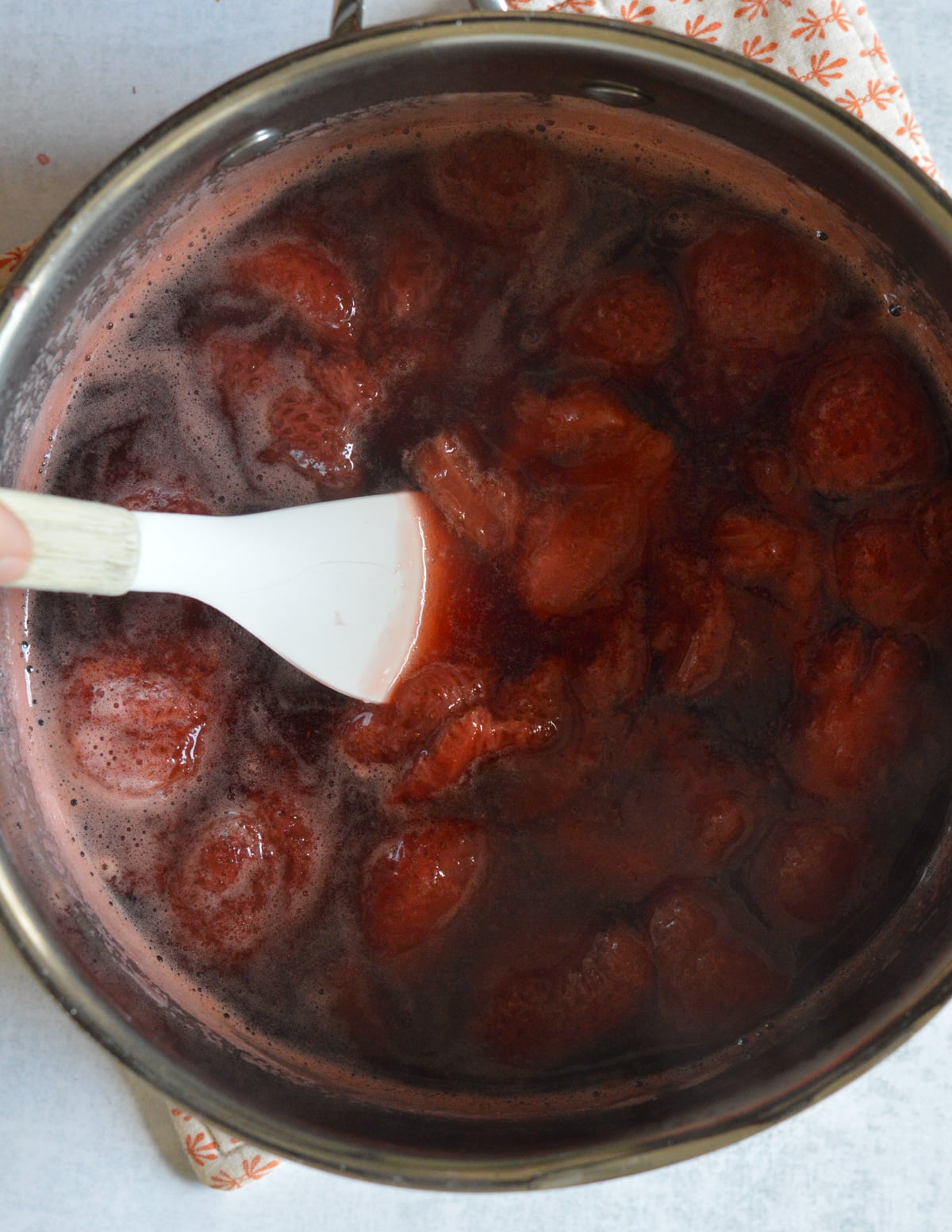 cooked strawberries in a saucepan with a spatula in it.