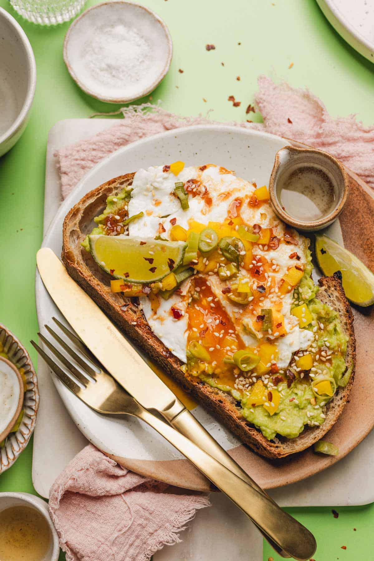 avocado toast with a fried egg, honey chipotle sauce, and pickled bell pepper on top.