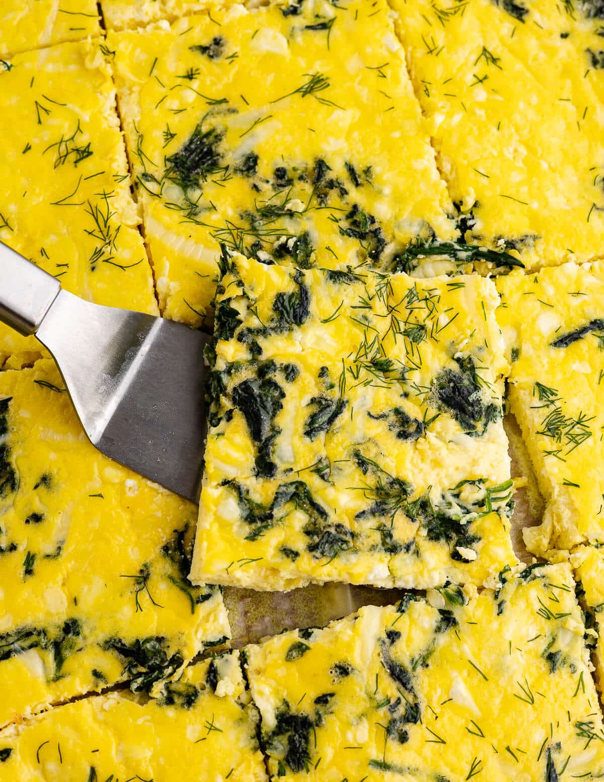 metal spatula holding a baked egg square with spinach and dill.