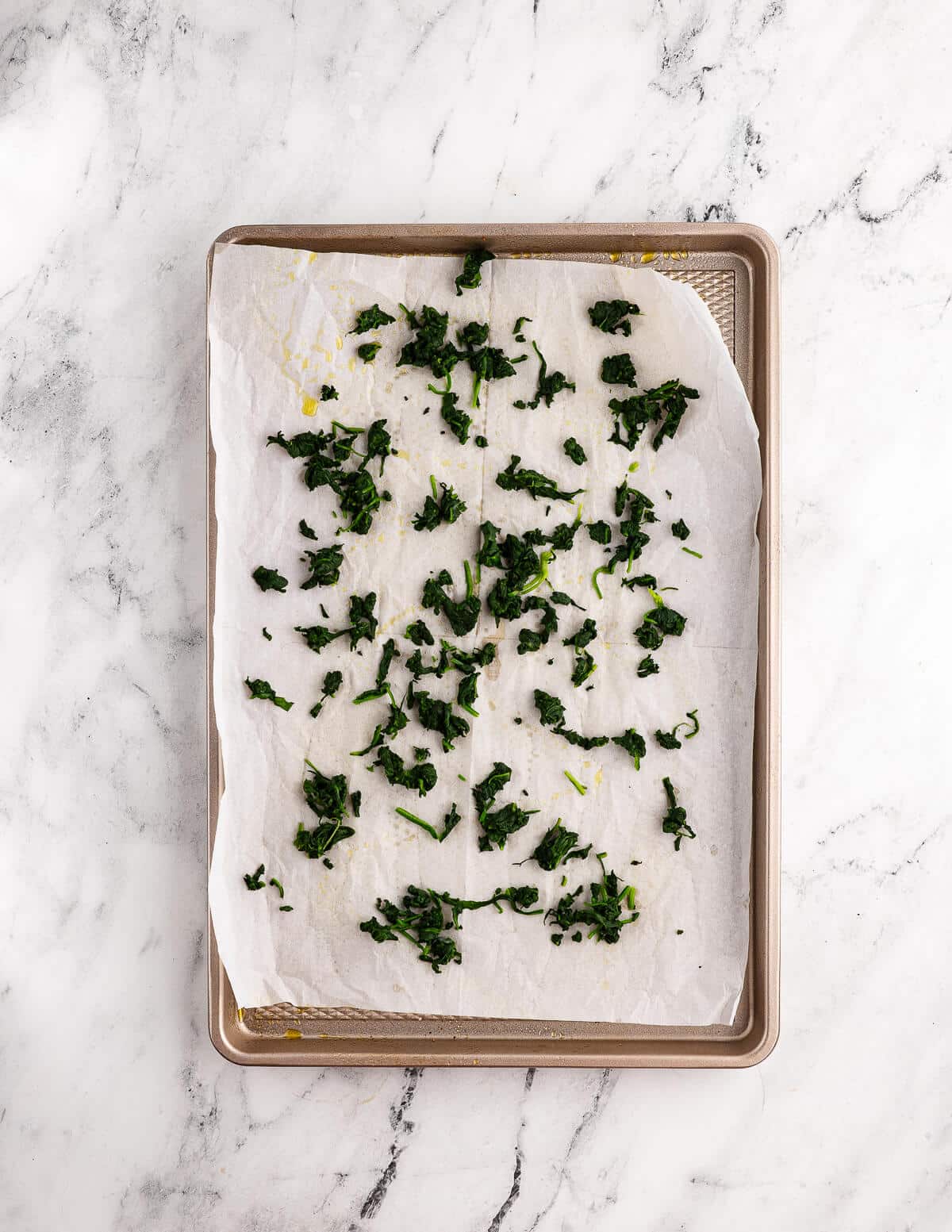 cooked spinach on parchment paper in a sheet pan.