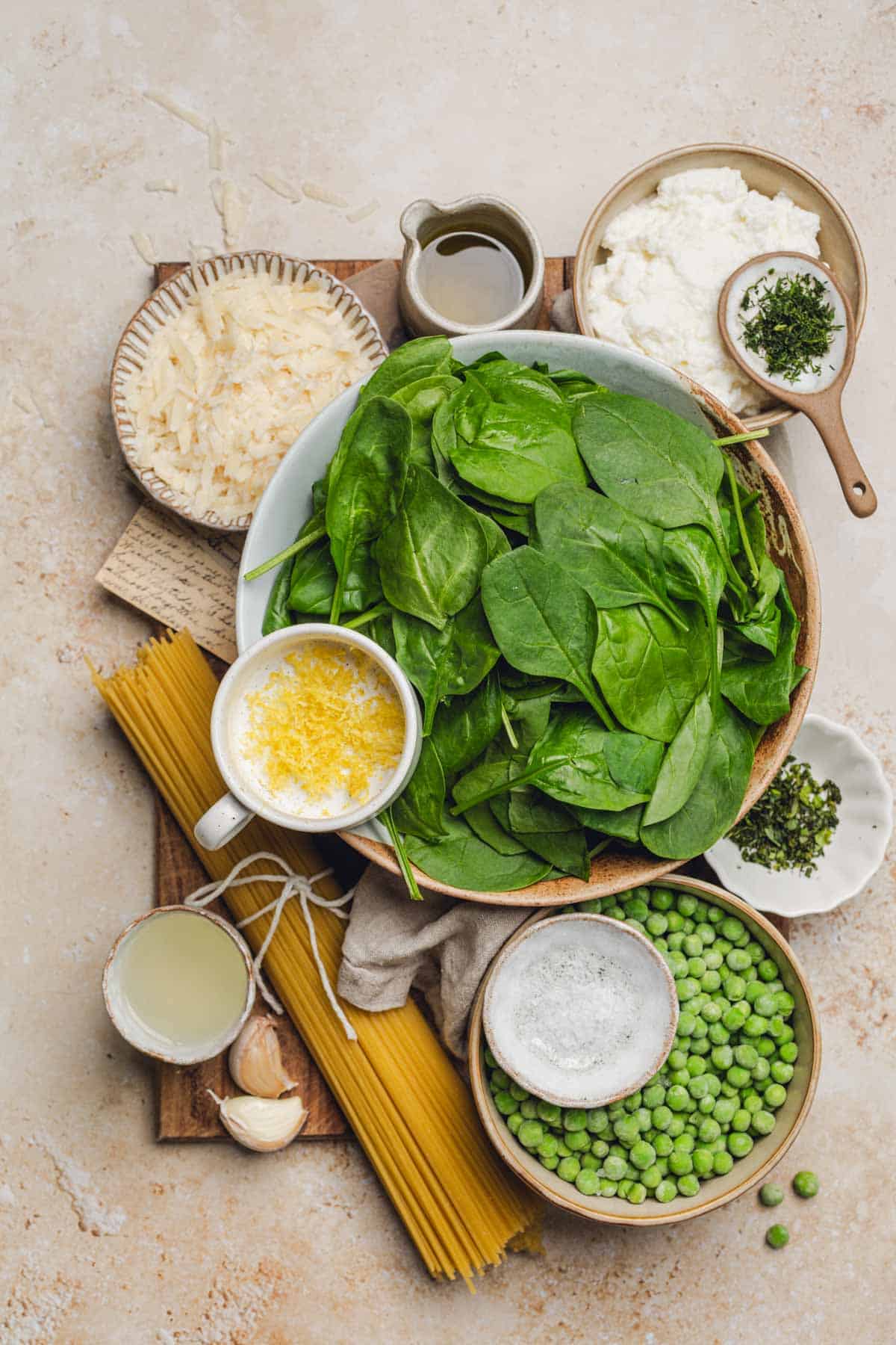 a bowl of spinach, lemon zest, parmesan, ricotta cheese, dill, peas, lemon juice, garlic, and spaghetti noodles.