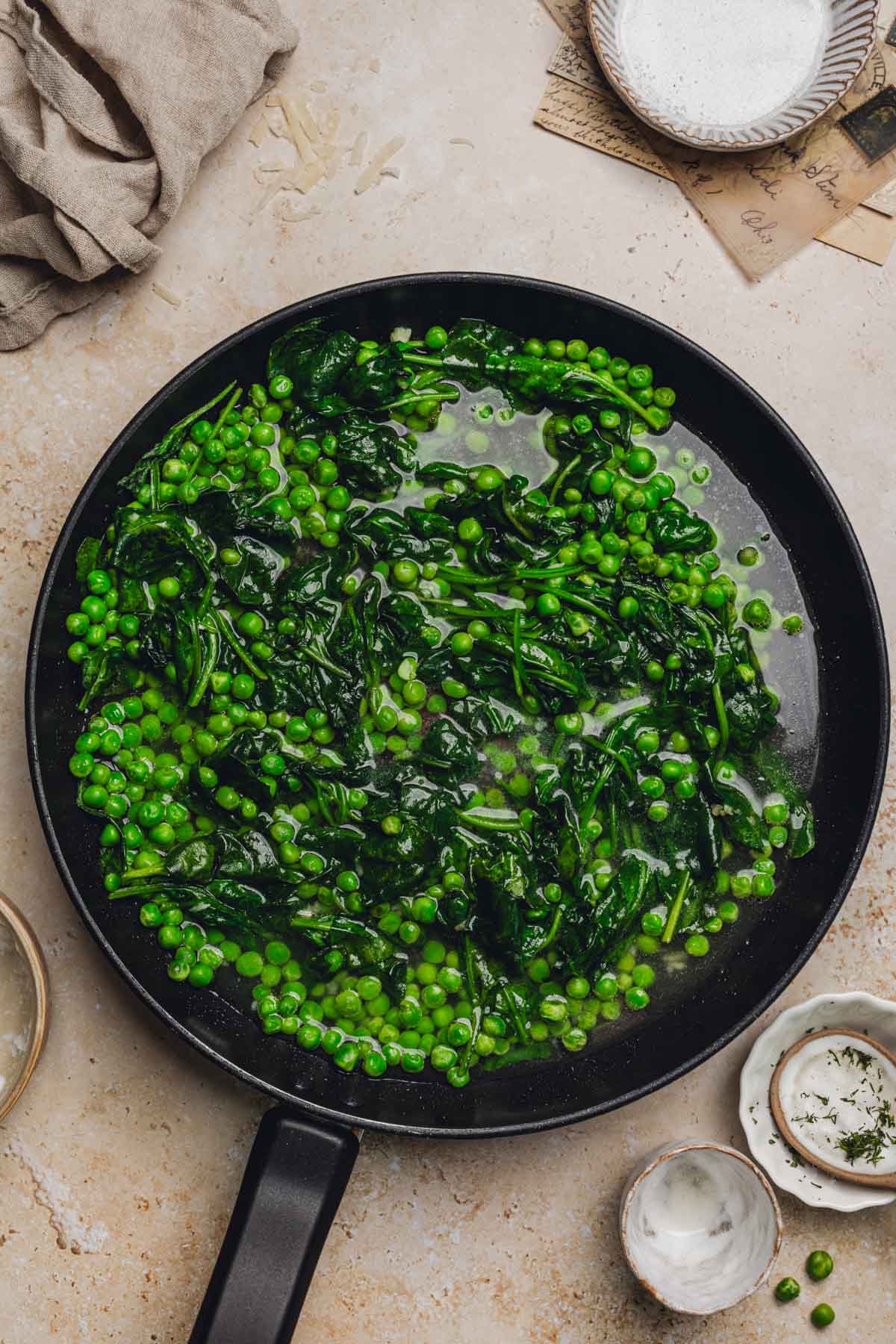 a skillet with cooked spinach, peas, and pasta water.