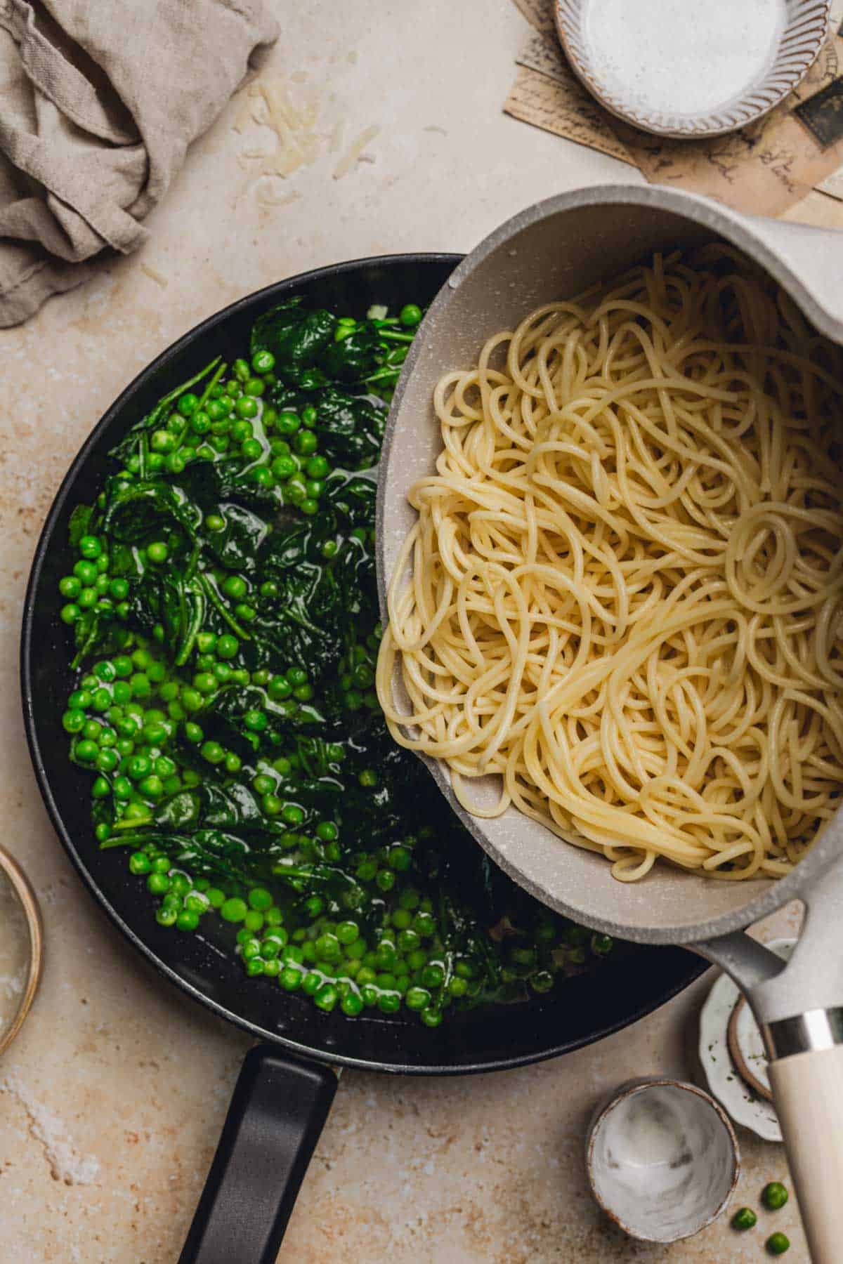 pouring the cooked pasta in the skillet with peas, spinach, and pasta water.