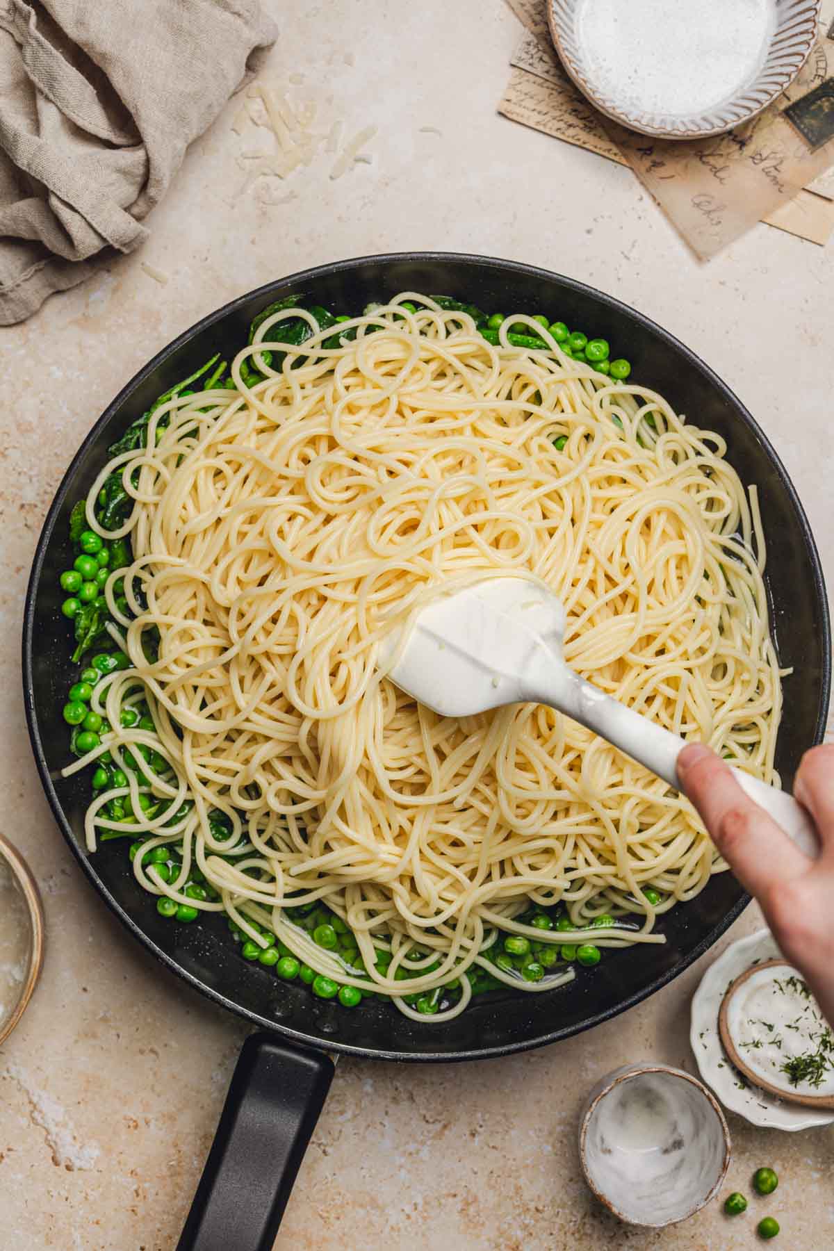 stirring pasta with a spatula in a skillet of spinach and peas.