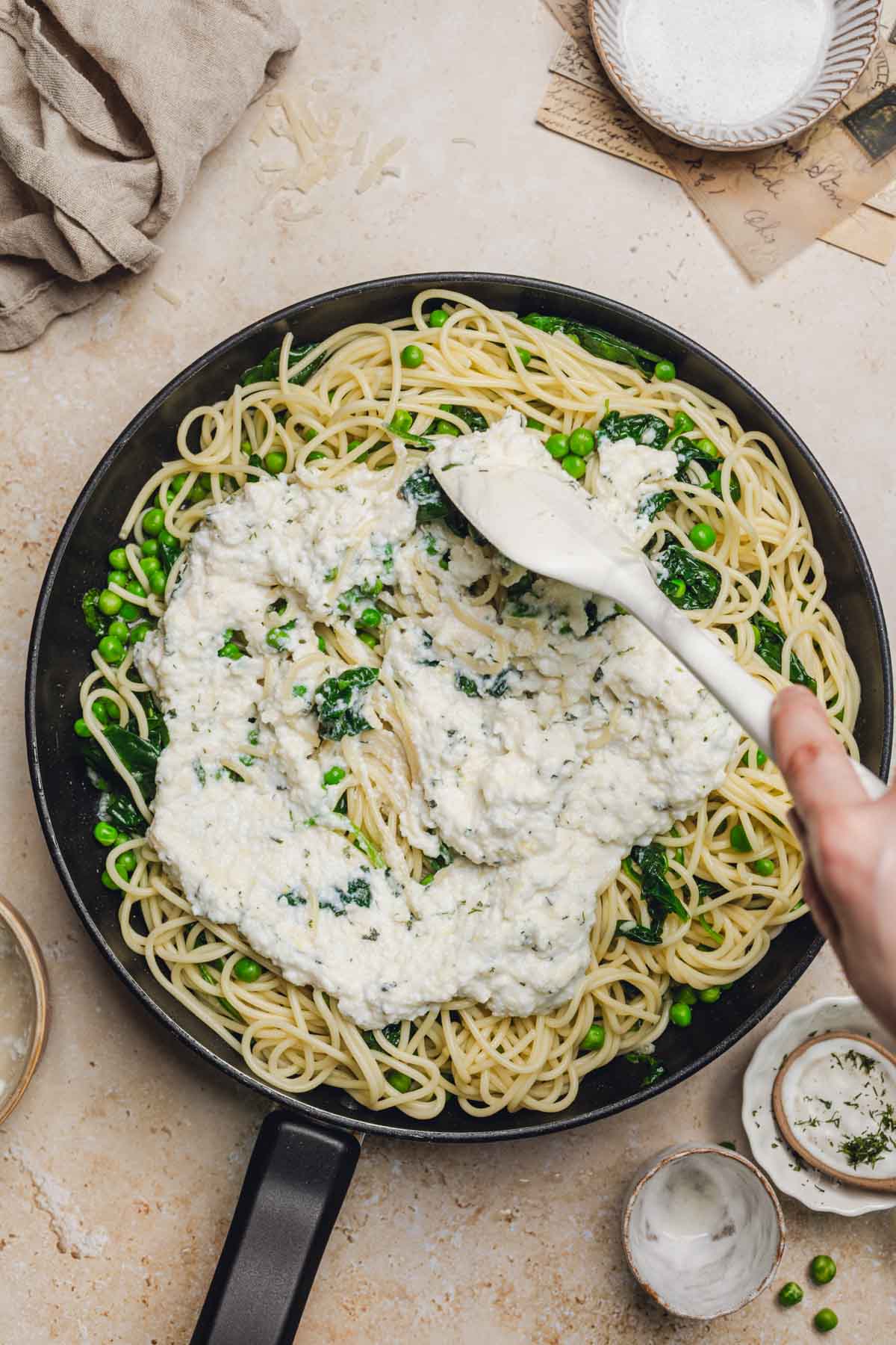 spatula stirring a ricotta parmesan sauce into a skillet with noodles and spinach.