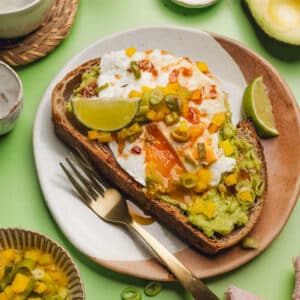 avocado toast on a plate with fried egg, chipotle sauce, and pickled bell peppers.