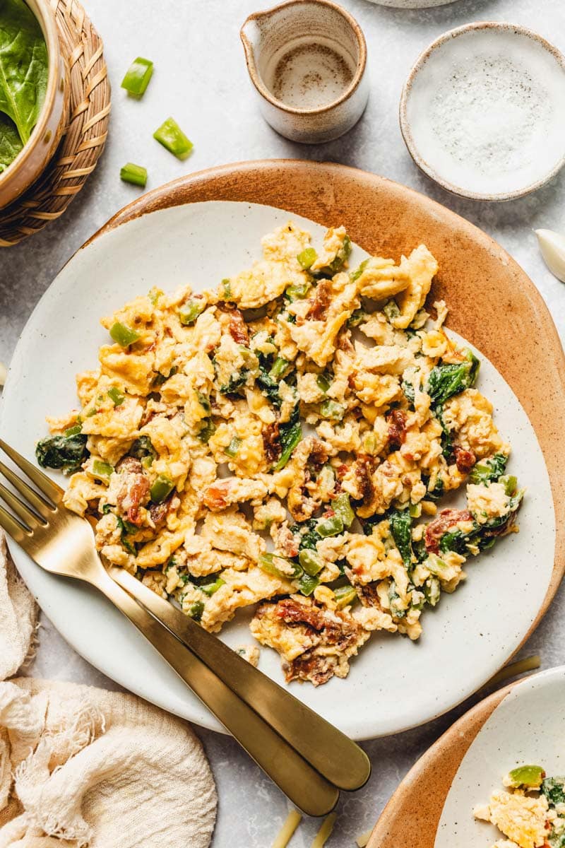 a plate of scrambled eggs with spinach, cheese, and sun-dried tomatoes.