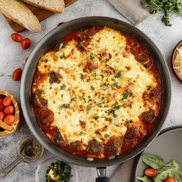 saucy meatballs in a skillet covered with melted cheese