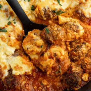 a spoonful of meatballs in sauce with cheese on top.