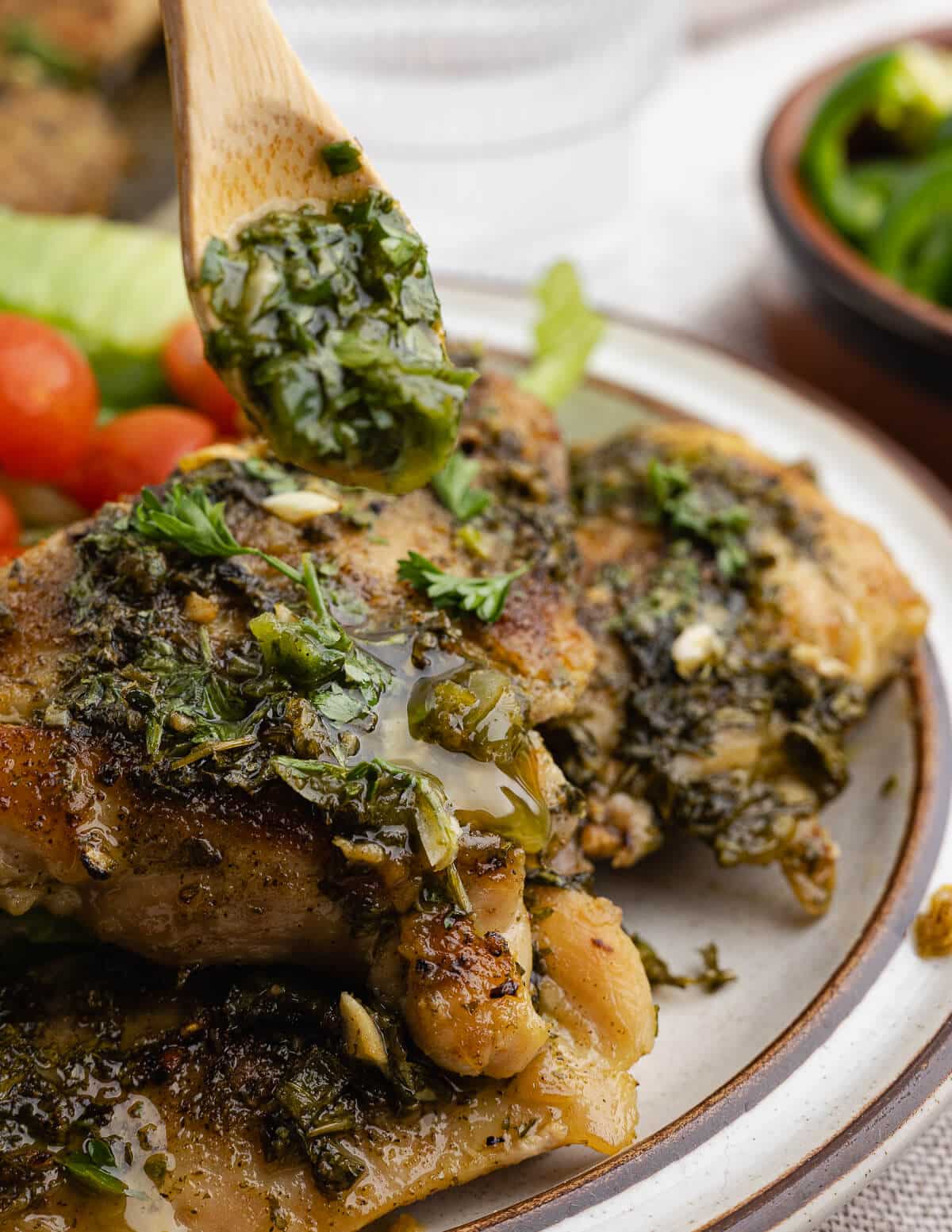 drizzling fresh chimichurri onto chimichurri chicken thighs