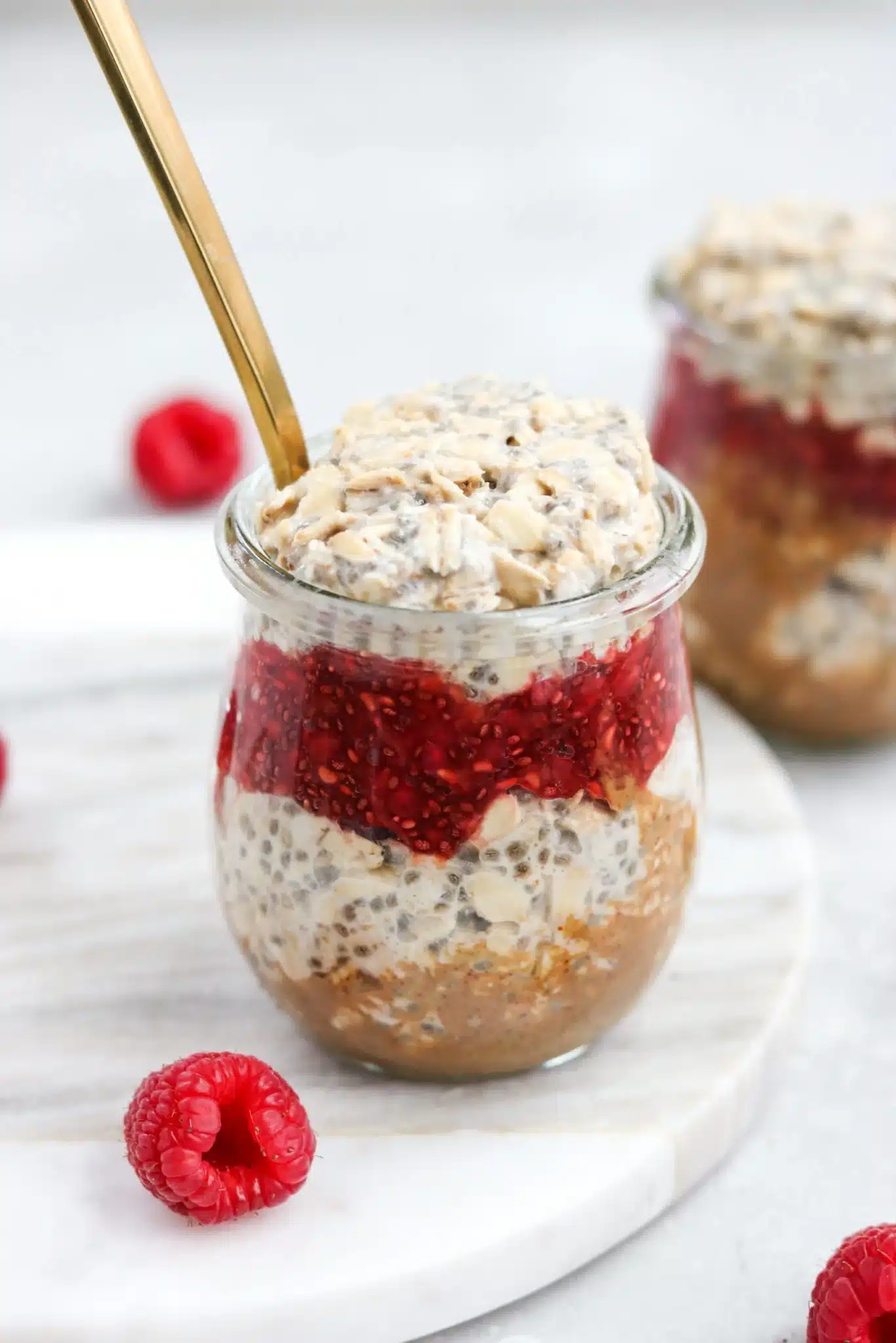 a jar full of almond butter, raspberry jam, and overnight oats.