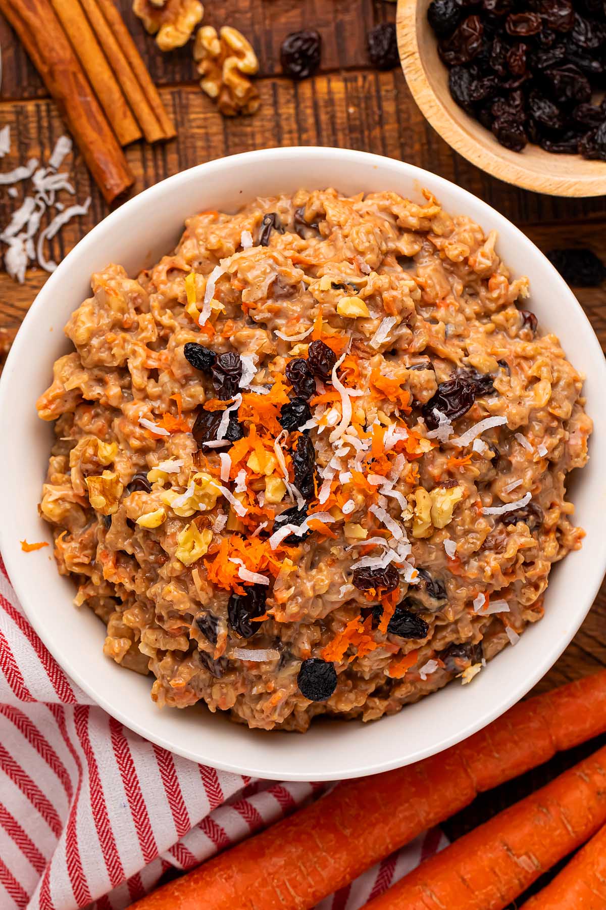 a bowl of carrot cake oatmeal with shredded carrots and raisins on top.