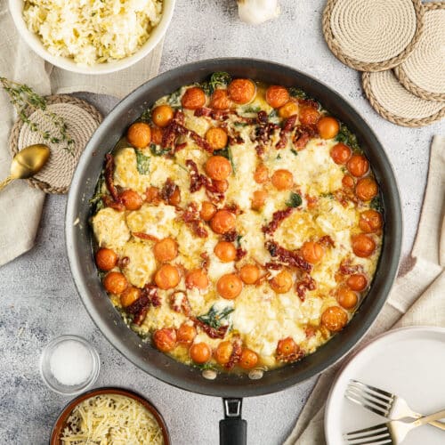 a skillet with chicken meatballs in a creamy sauce with tomatoes.