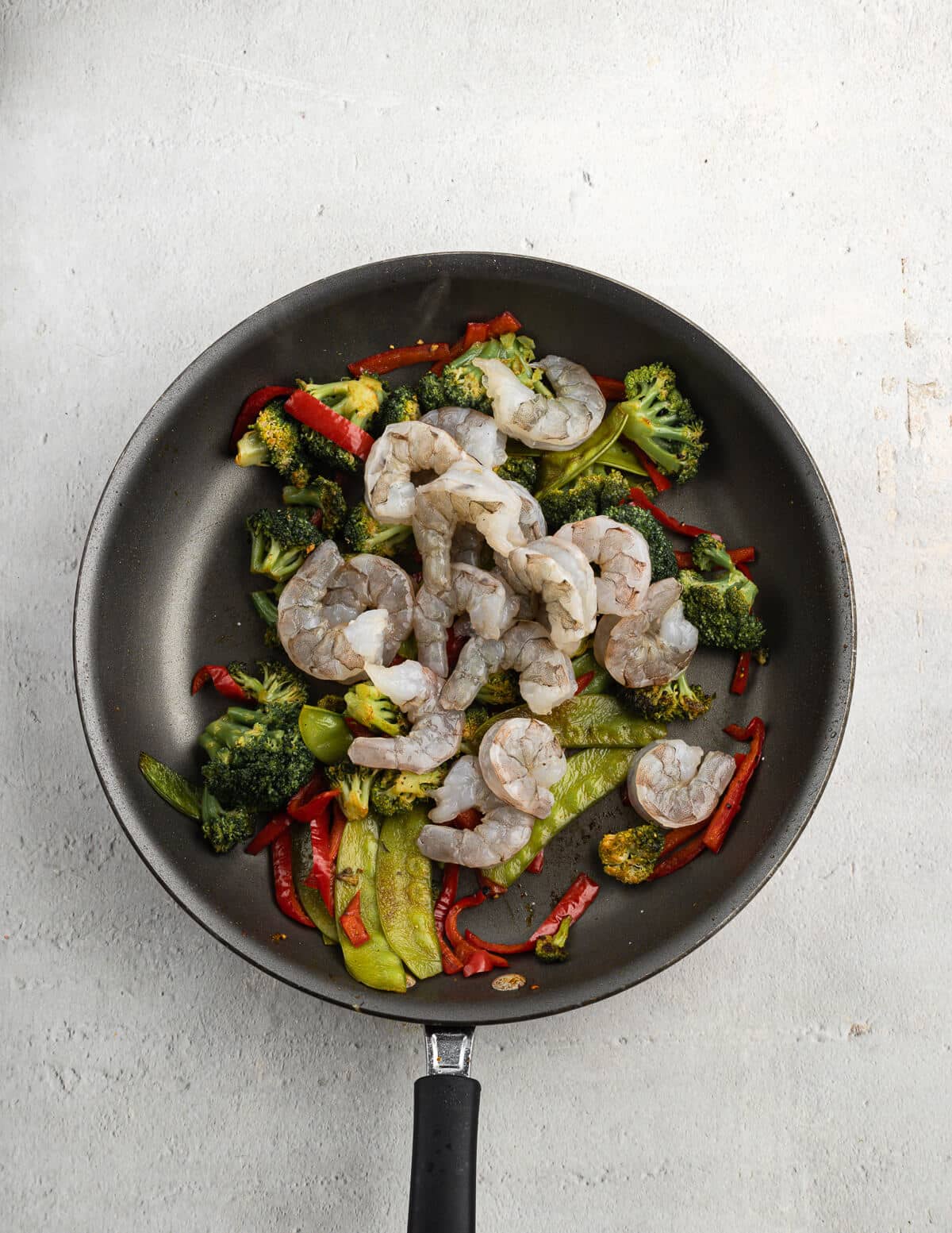 sautéed veggies and raw shrimp in a skillet.
