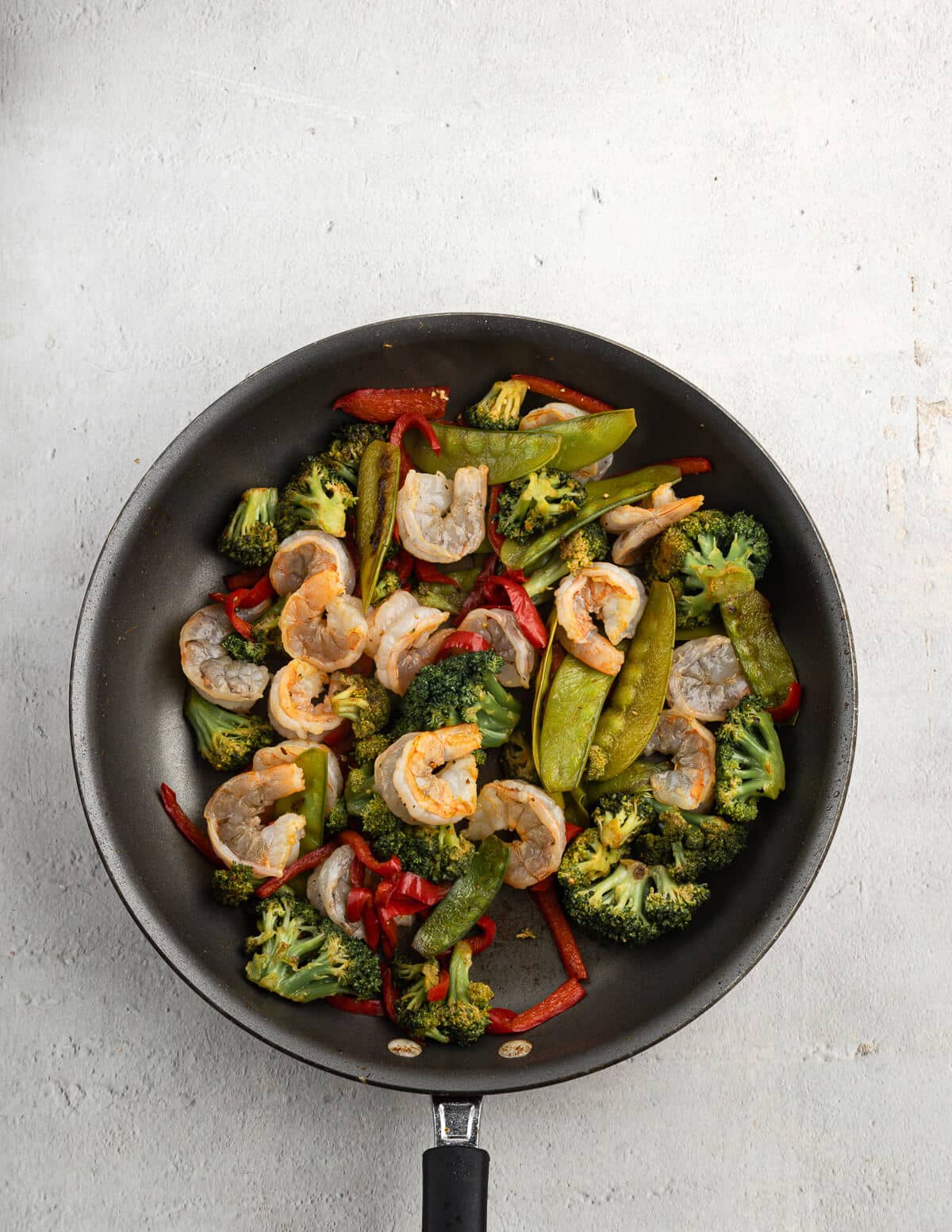 sauteed veggies and partially cooked shrimp in a skillet.