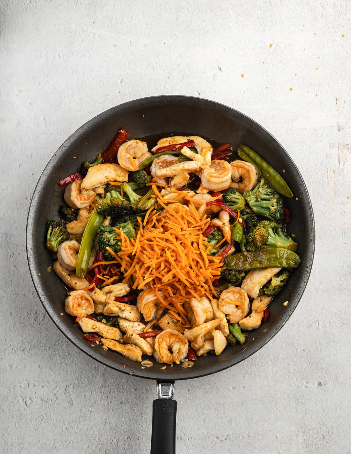 cooked shrimp and sauteed veggies in a skillet with matchstick carrots on top.