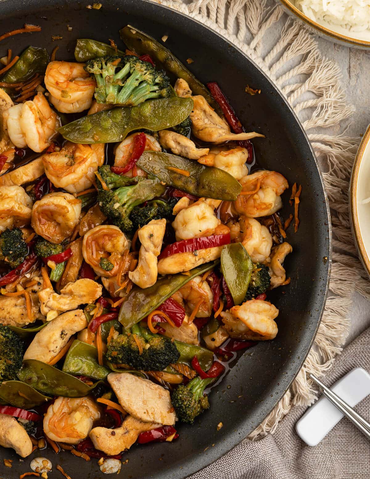 a skillet with chicken and shrimp stir fry with veggies.