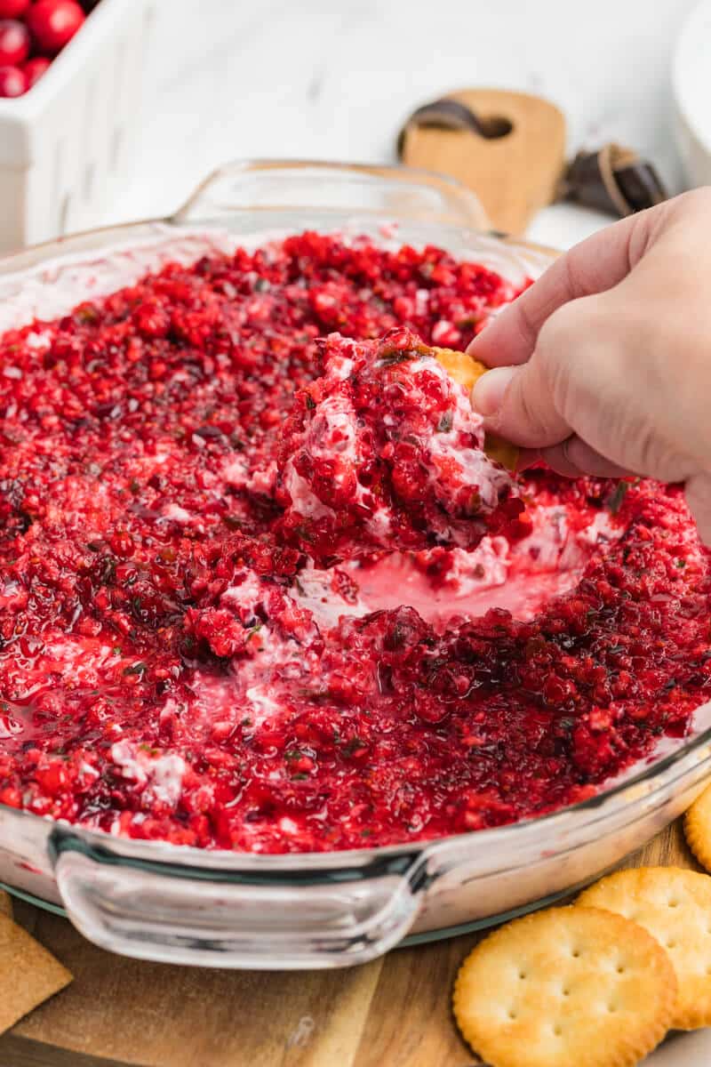 hand scooping cranberry cream cheese dip onto a ritz cracker