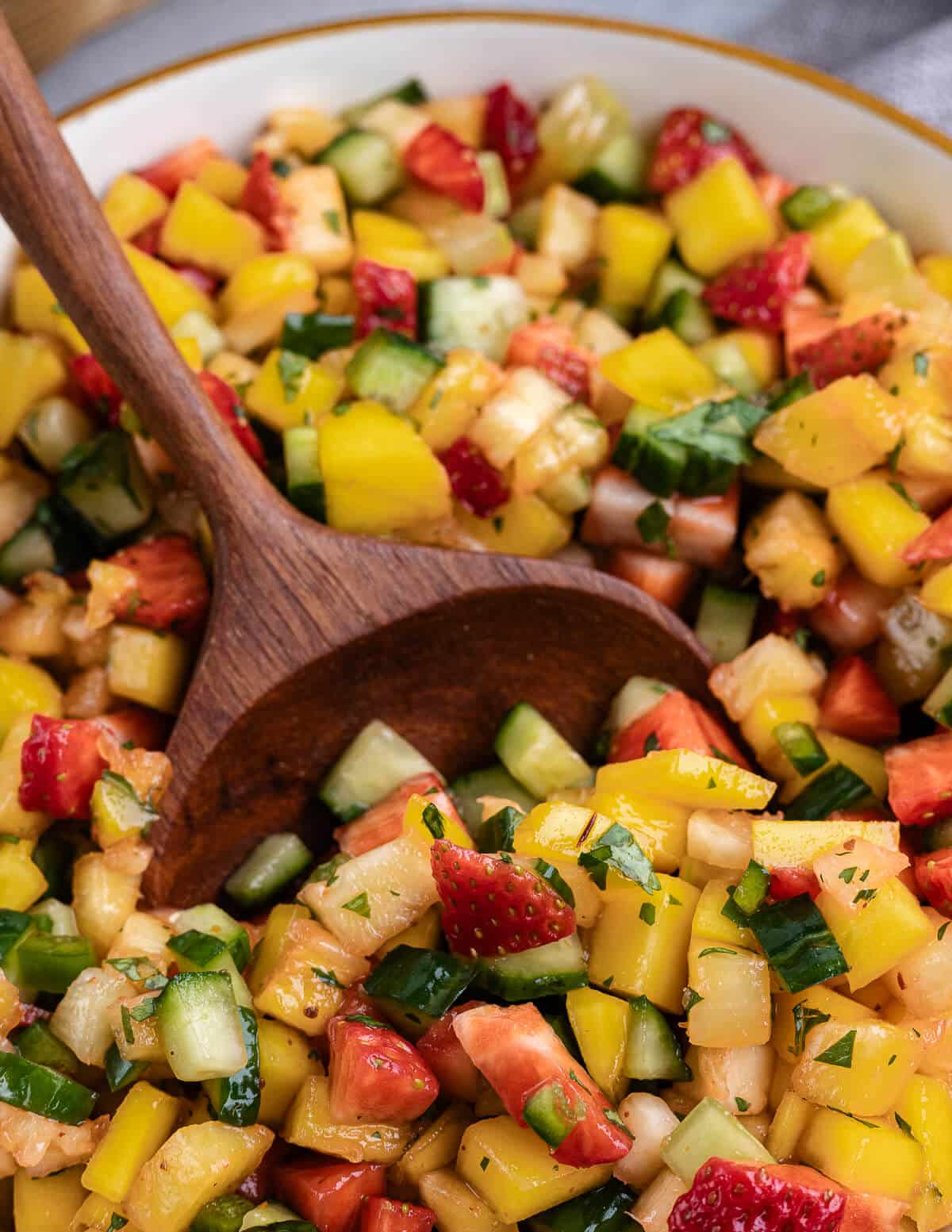 a wooden spoon scooping up fruit salsa with cucumbers and strawberries.