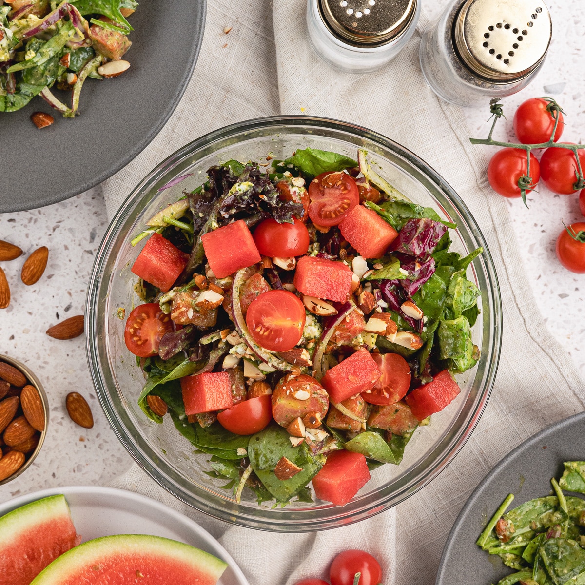 a bowl of watermelon salad with watermelon, greens, tomatoes, and goat cheese.