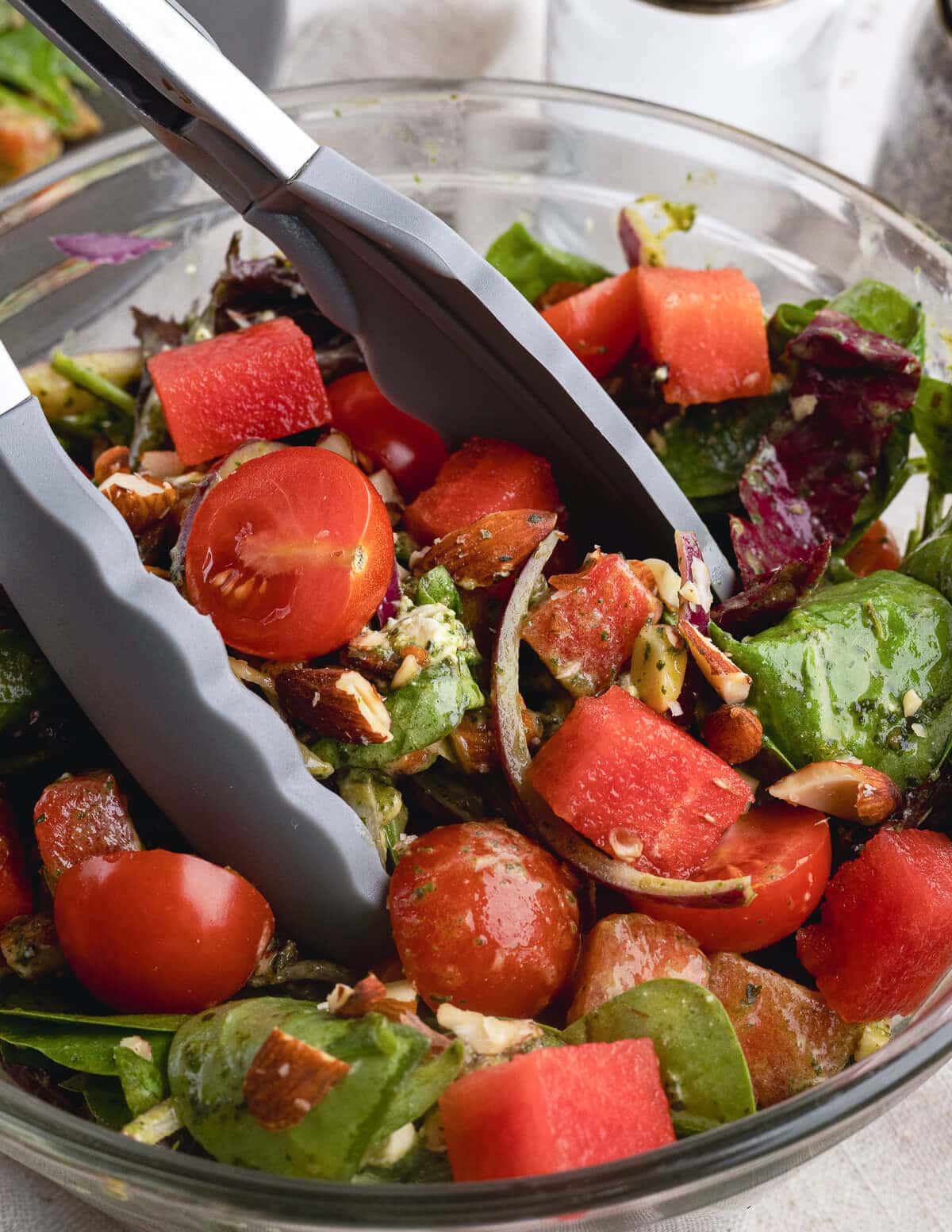 a salad with watermelon, cherry tomatoes, red onion, roasted almonds, and goat cheese in a honey basil vinaigrette