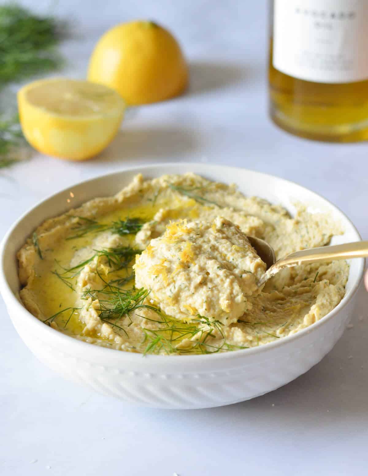 a bowl of lemon dill hummus with a spoonful of it