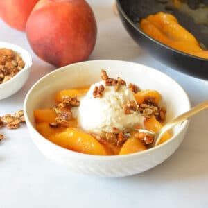 a bowl of candied peaches with vanilla ice cream and candied pepitas.