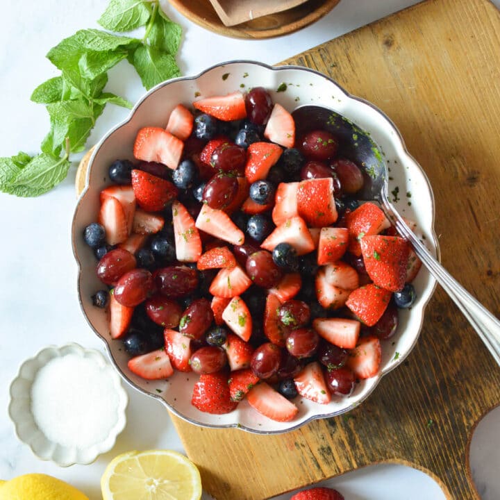 a bowl of strawberry fruit salad with mint, grapes, and blueberries.