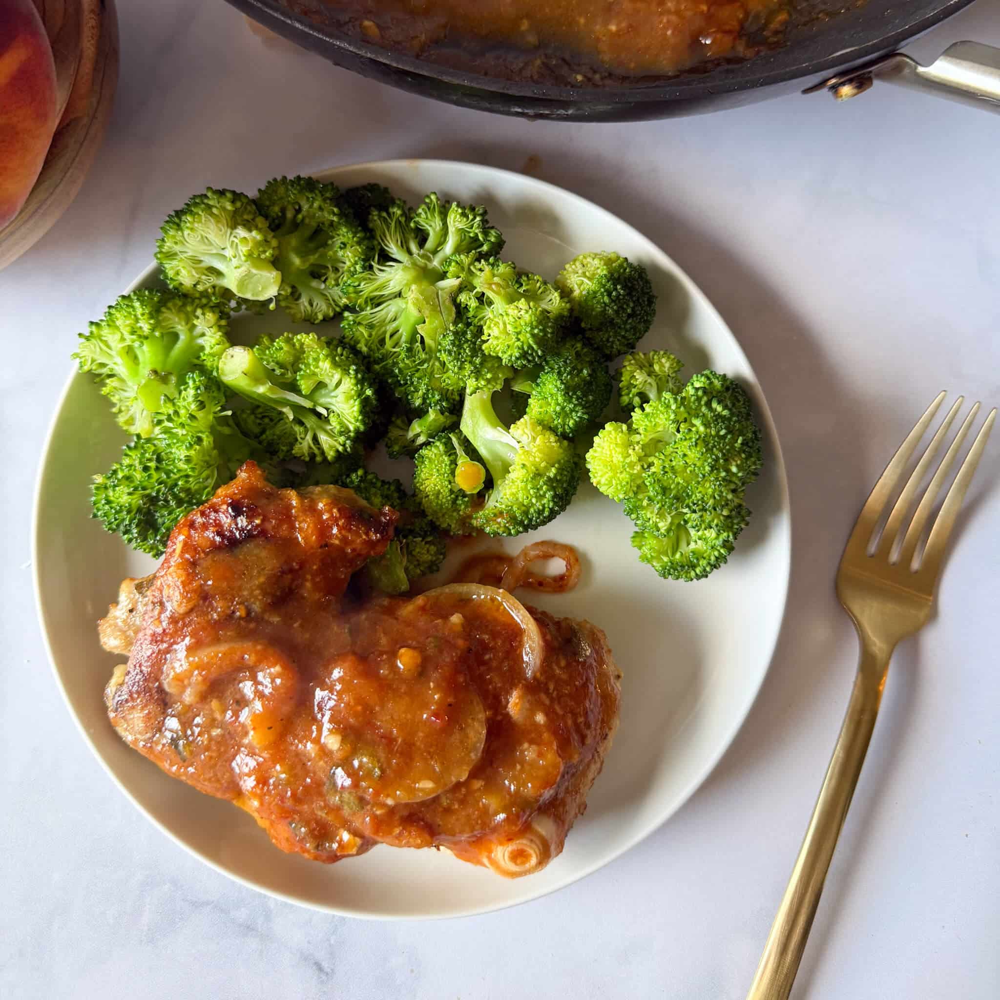 a plate of peach chipotle chicken thighs with steamed broccoli.