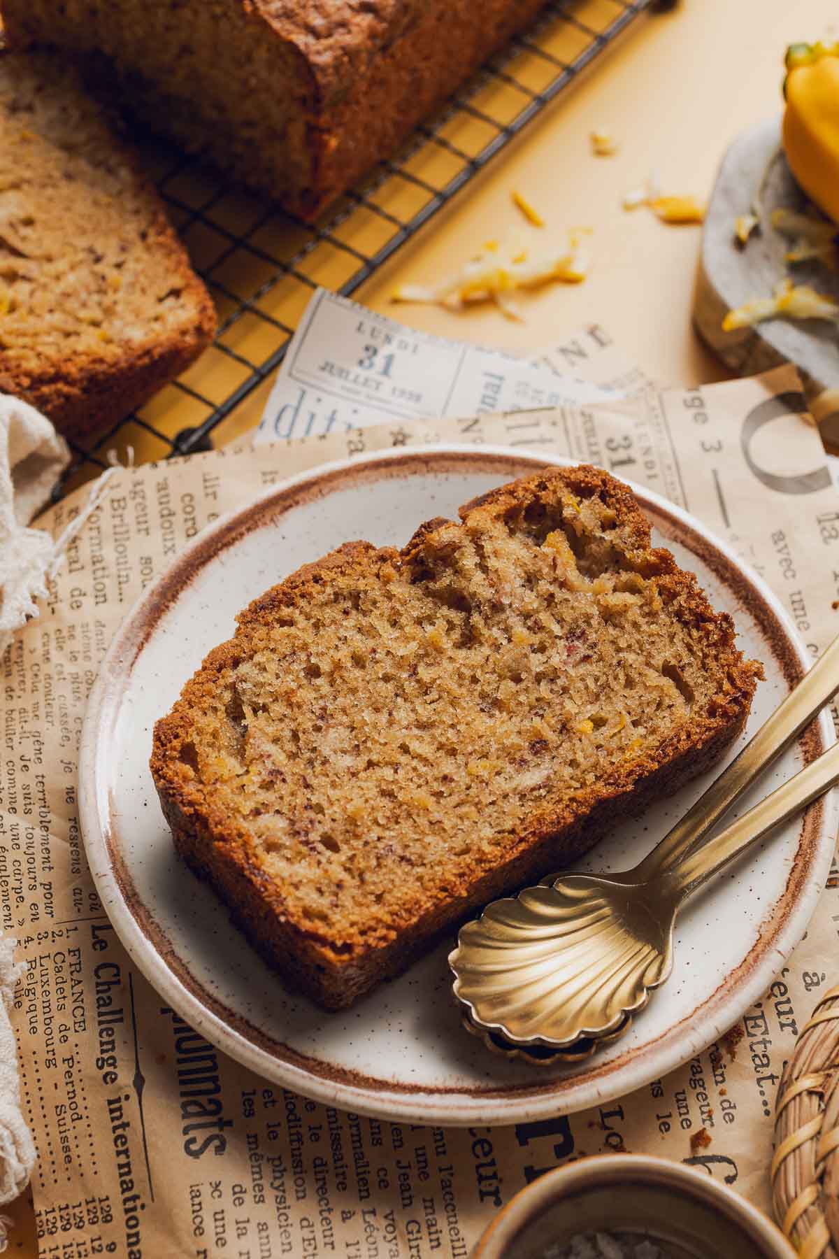 a slice of yellow squash bread on a plate with golden spoons next to it.